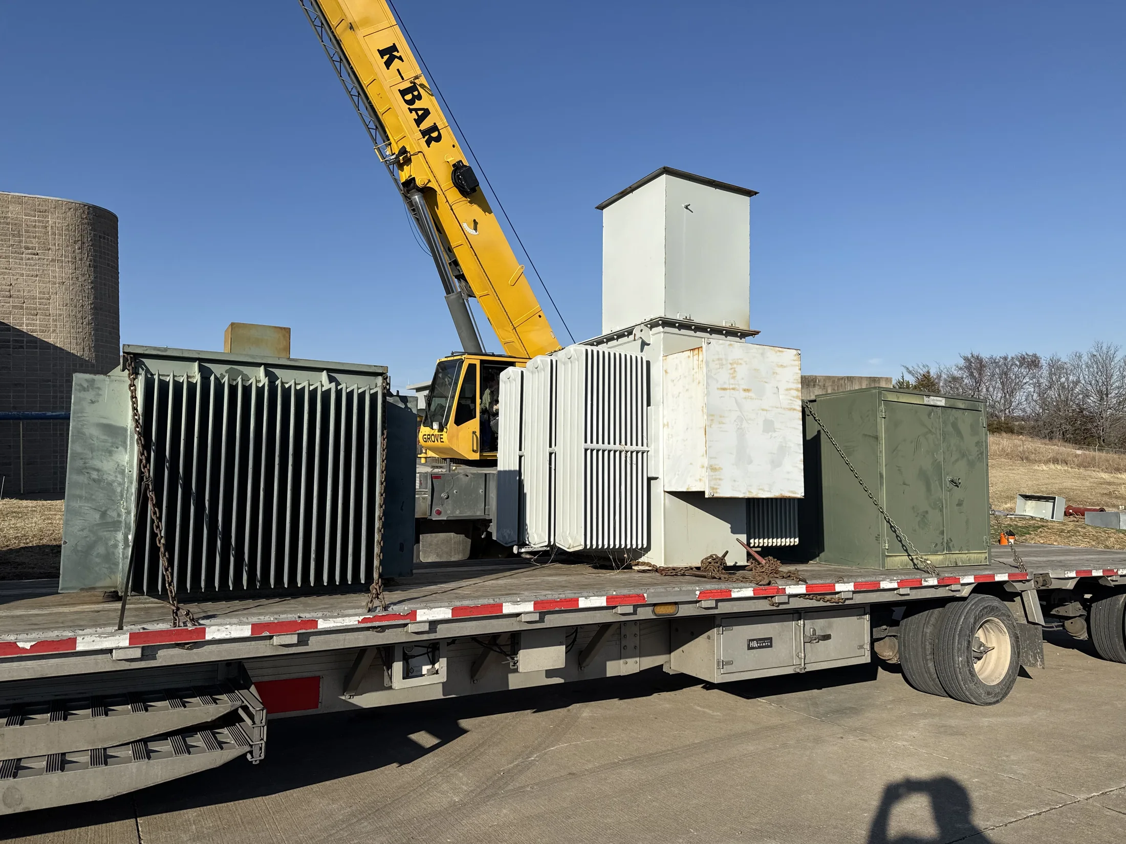 Multiple surplus transformers staged with a crane and flatbed trailer